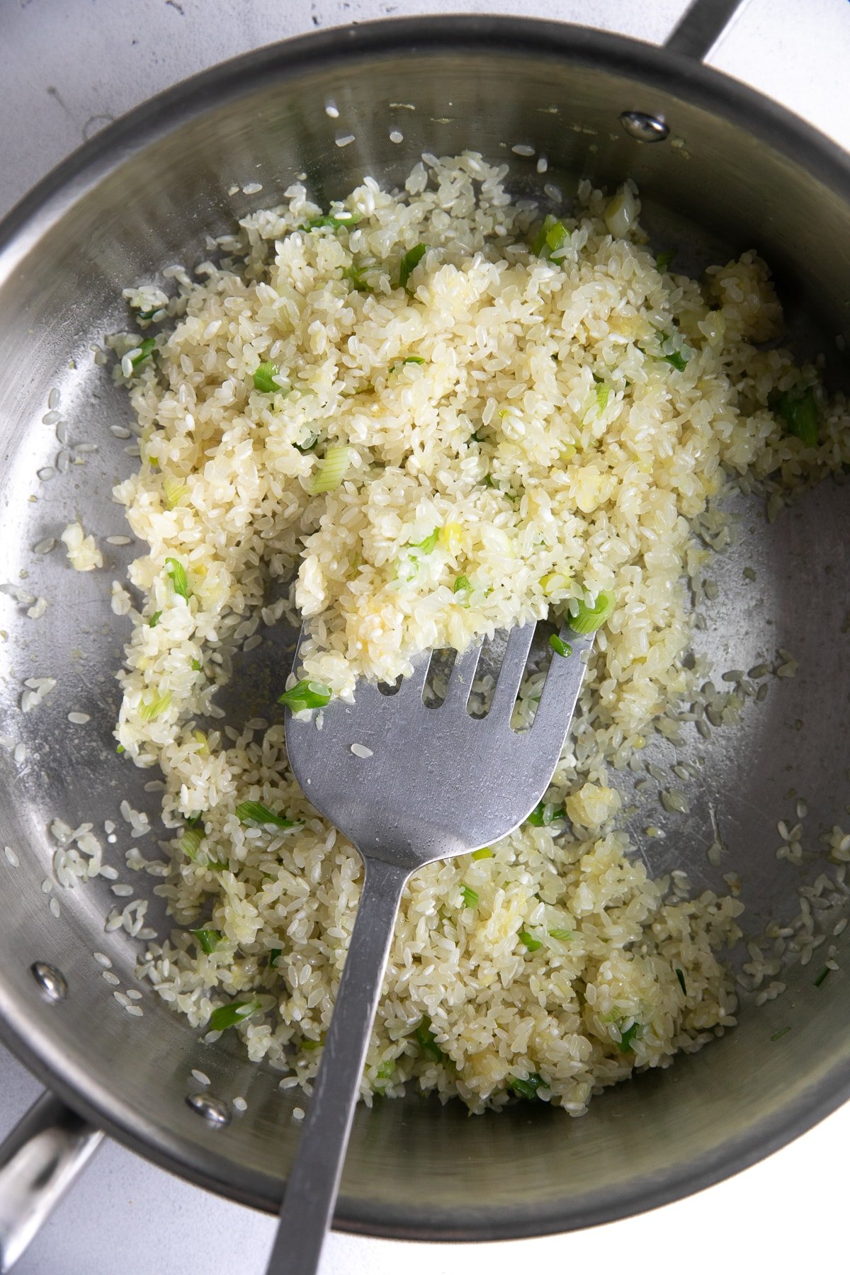 Browning rice in a hot skillet with ginger, garlic, and green onions.