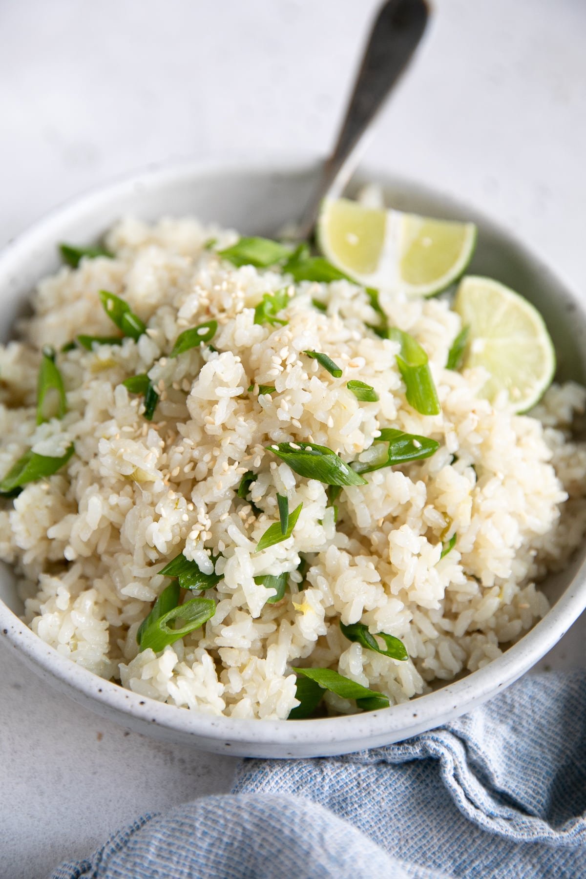 Coconut rice in a large white bowl garnished with sesame seeds and chopped green onions.