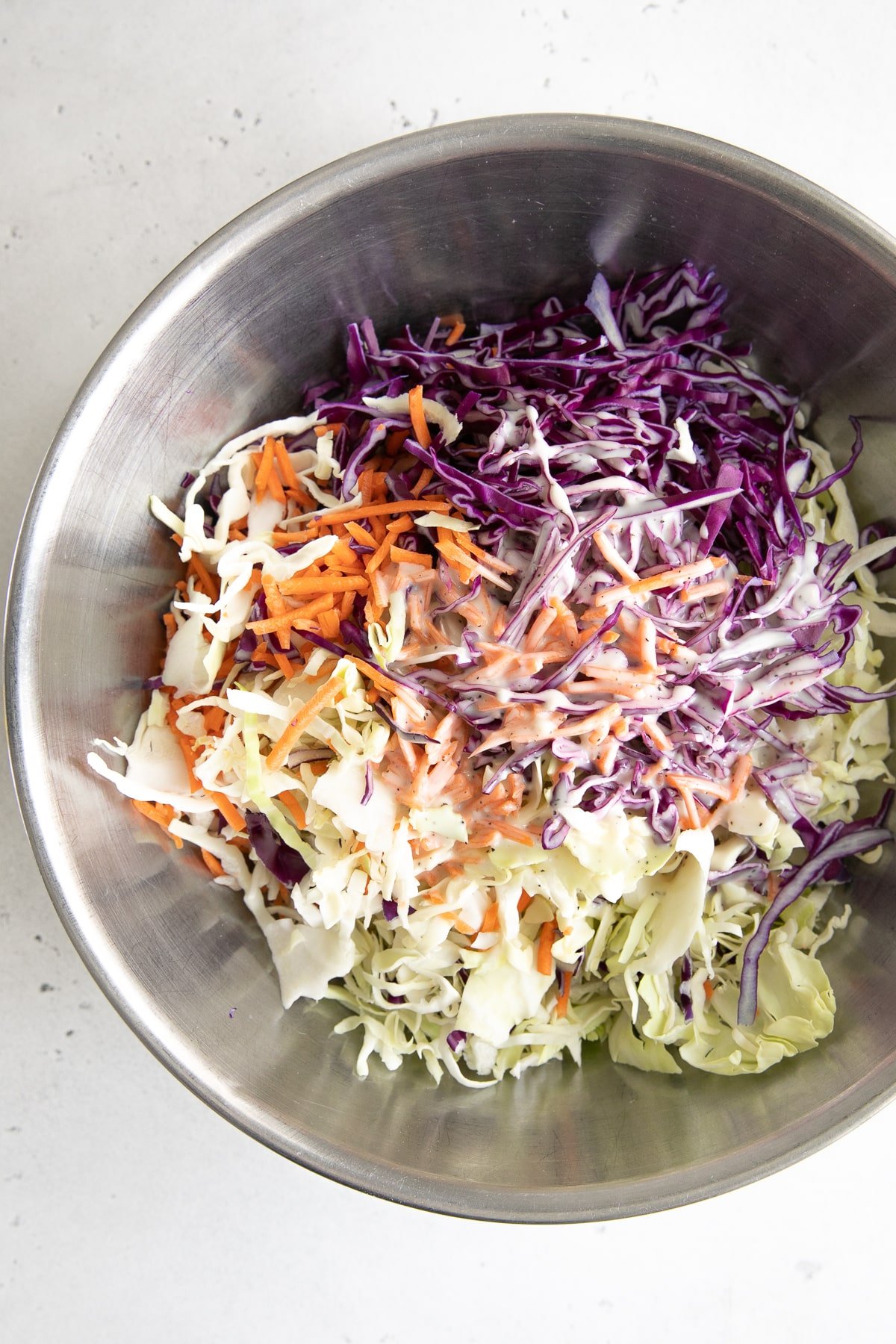 Large mixing bowl filled with shredded cabbage and carrots soaked in creamy coleslaw dressing.