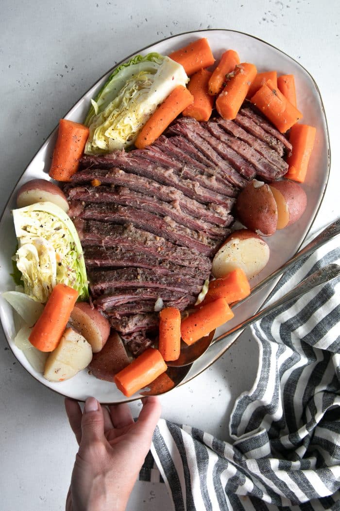 Large cooked and sliced corned beef brisket served on a large platter with carrots, potatoes, and cabbage.