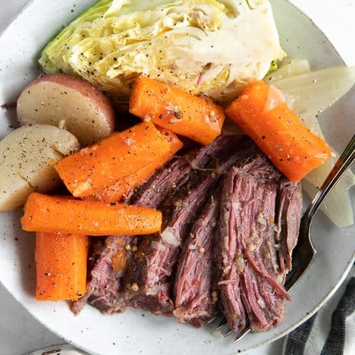 Dinner plate filled with slices of corned beef, carrots, potatoes, and cabbage wedges.