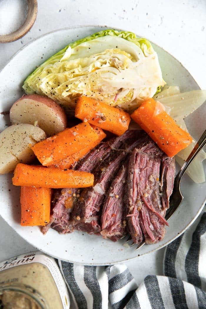 Dinner plate filled with slices of corned beef, carrots, potatoes, and cabbage wedges.