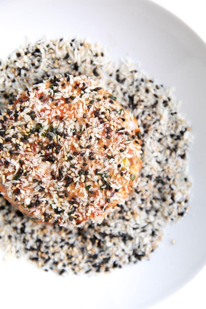 Coating raw salmon patty in a mixture of panko breadcrumbs, black sesame seeds, and white sesame seeds.