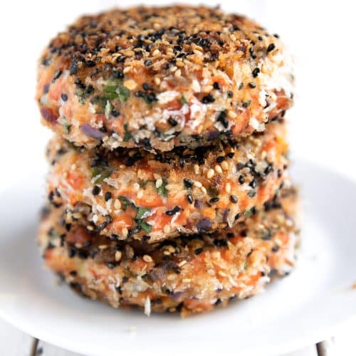 Three fully cooked salmon burger patties crusted with black and white sesame seeds.