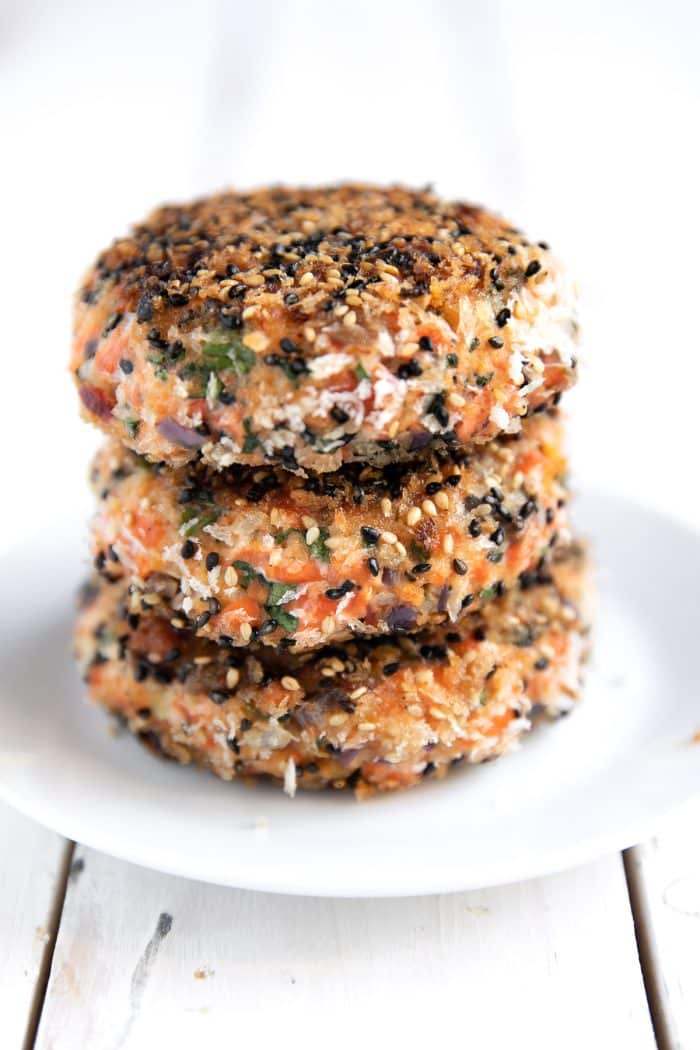 Three fully cooked salmon burger patties crusted with black and white sesame seeds.