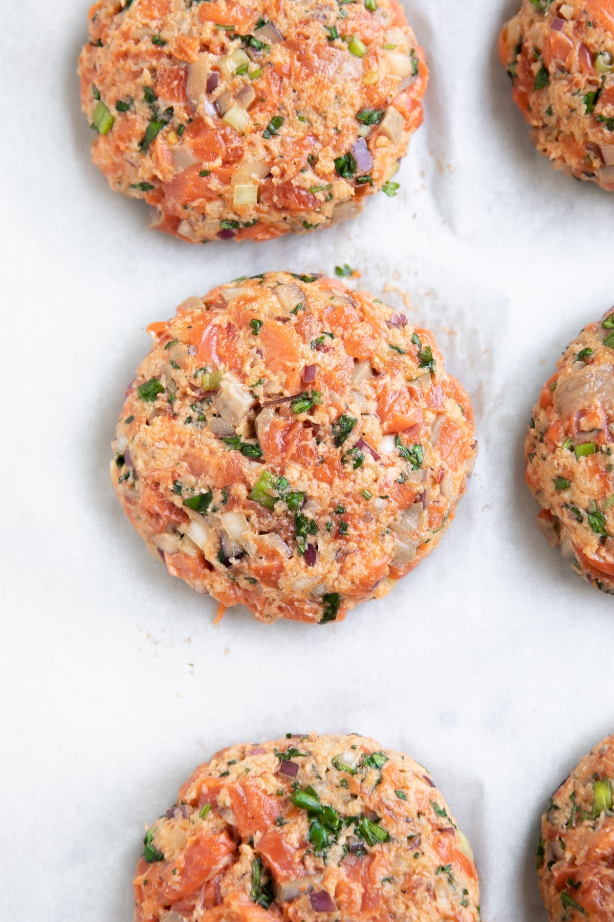Six raw salmon patties on a large parchment-paper lined baking sheet.