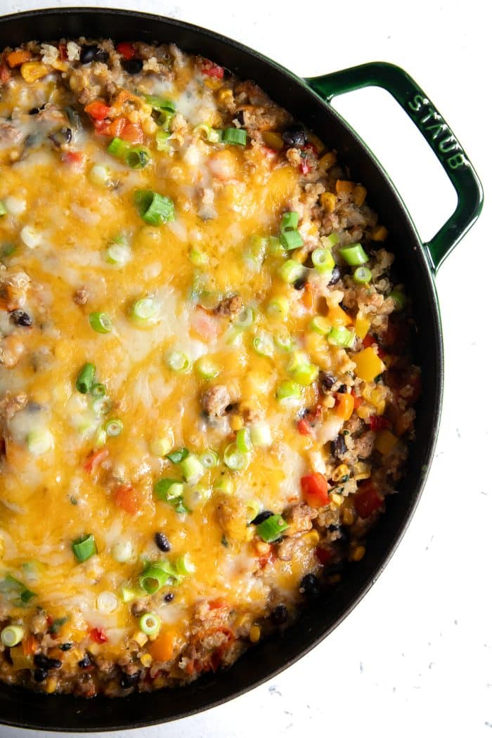 Large cast iron skillet filled with cheesy baked quinoa mixed with fresh veggies, black beans, corn, and ground chicken.