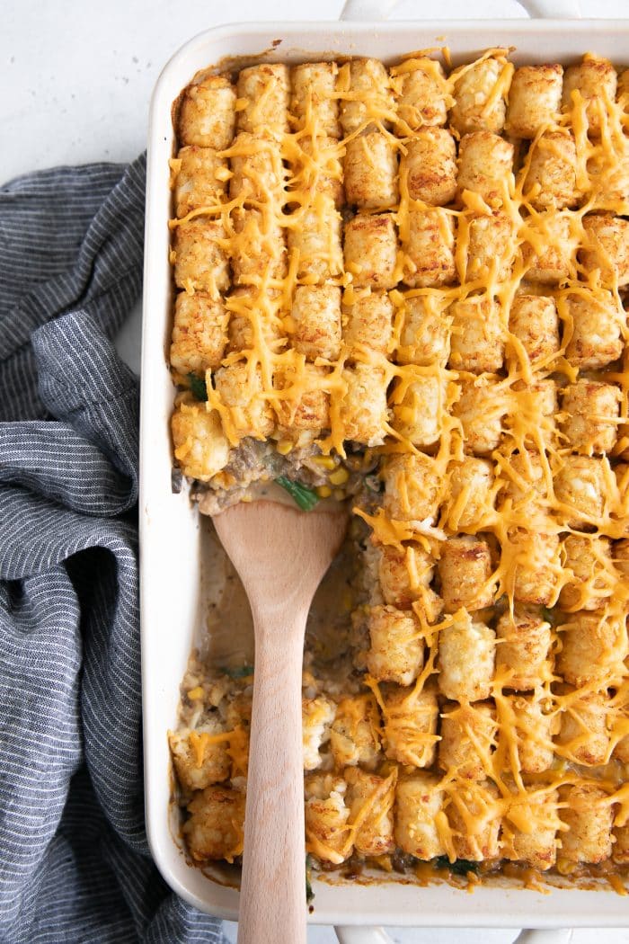 Overhead image of a baked tater tot casserole with single serving scooped from the middle.