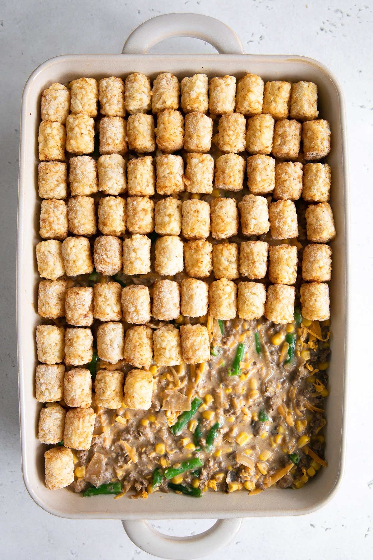 Placing frozen tater tots on top of the tater tot casserole meat mixture.