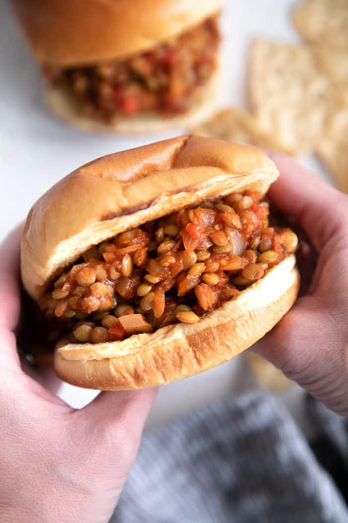 Hands holding a vegetarian sloppy joe made with lentils, onion, and bell pepper.