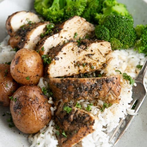 Sliced chicken breast and potatoes served over rice with cooked broccoli.