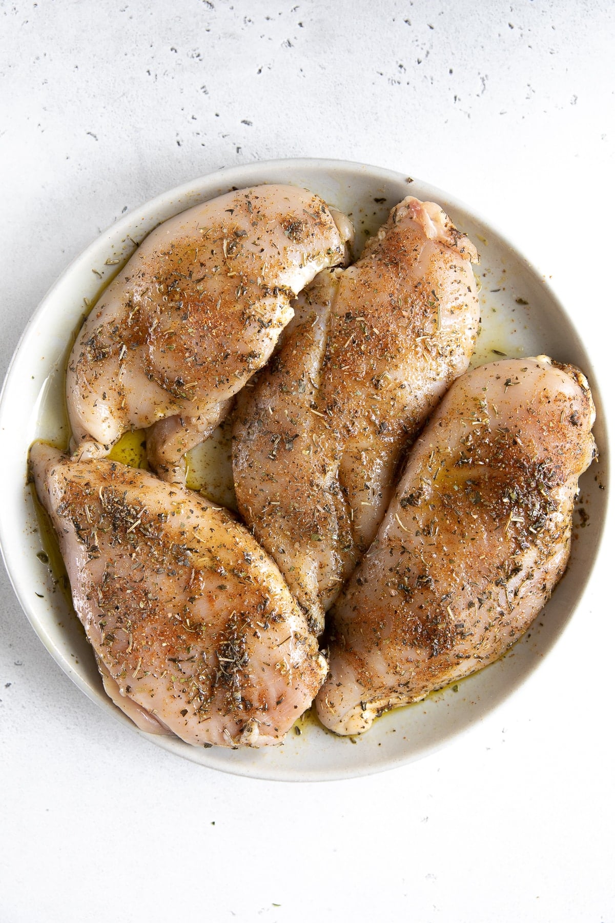 Four seasoned chicken breasts on a large plate.