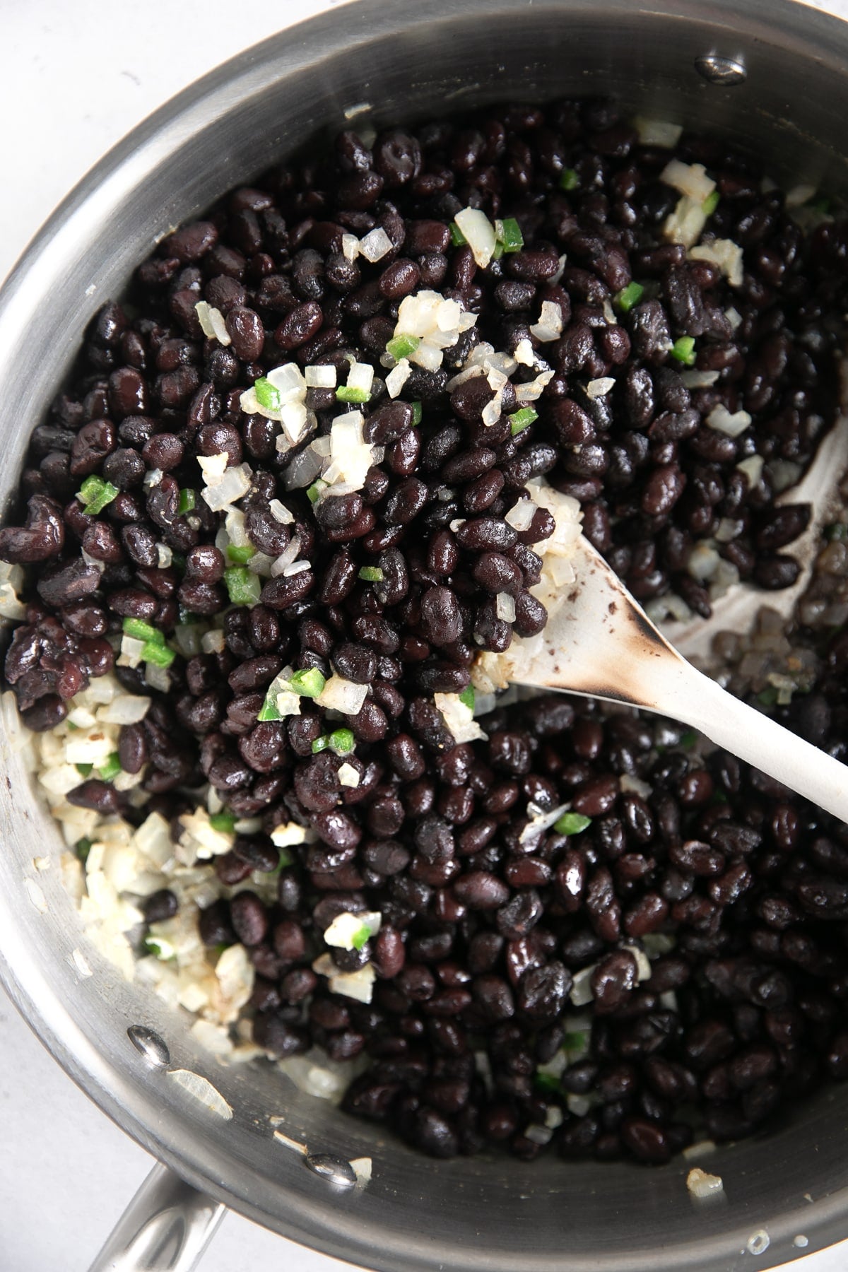 Mixing cooked black beans with sauteed onions, garlic, and jalapeno in a medium pan.