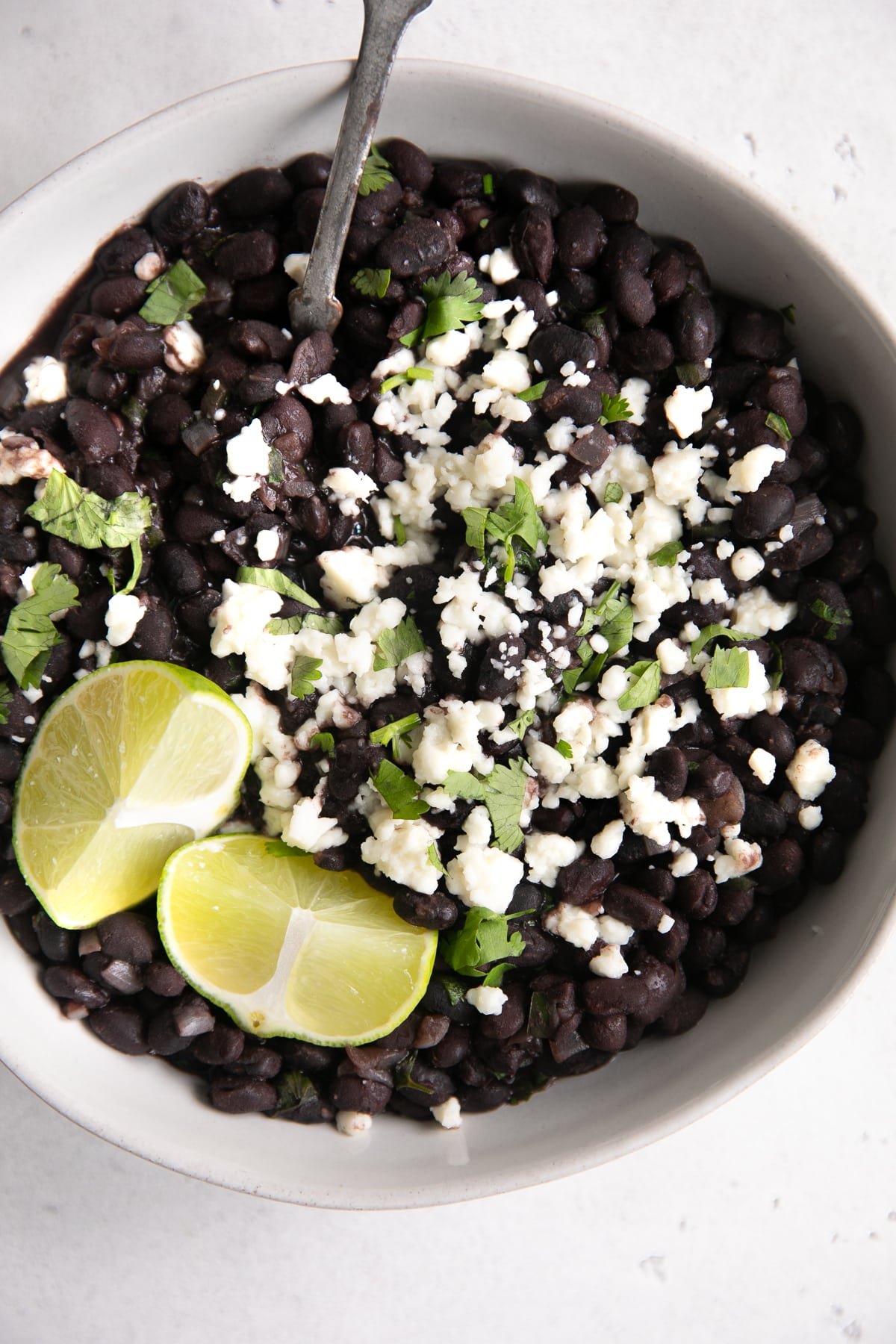 White bowl filled with Mexican-style black beans garnished with cotija cheese and fresh cilantro.