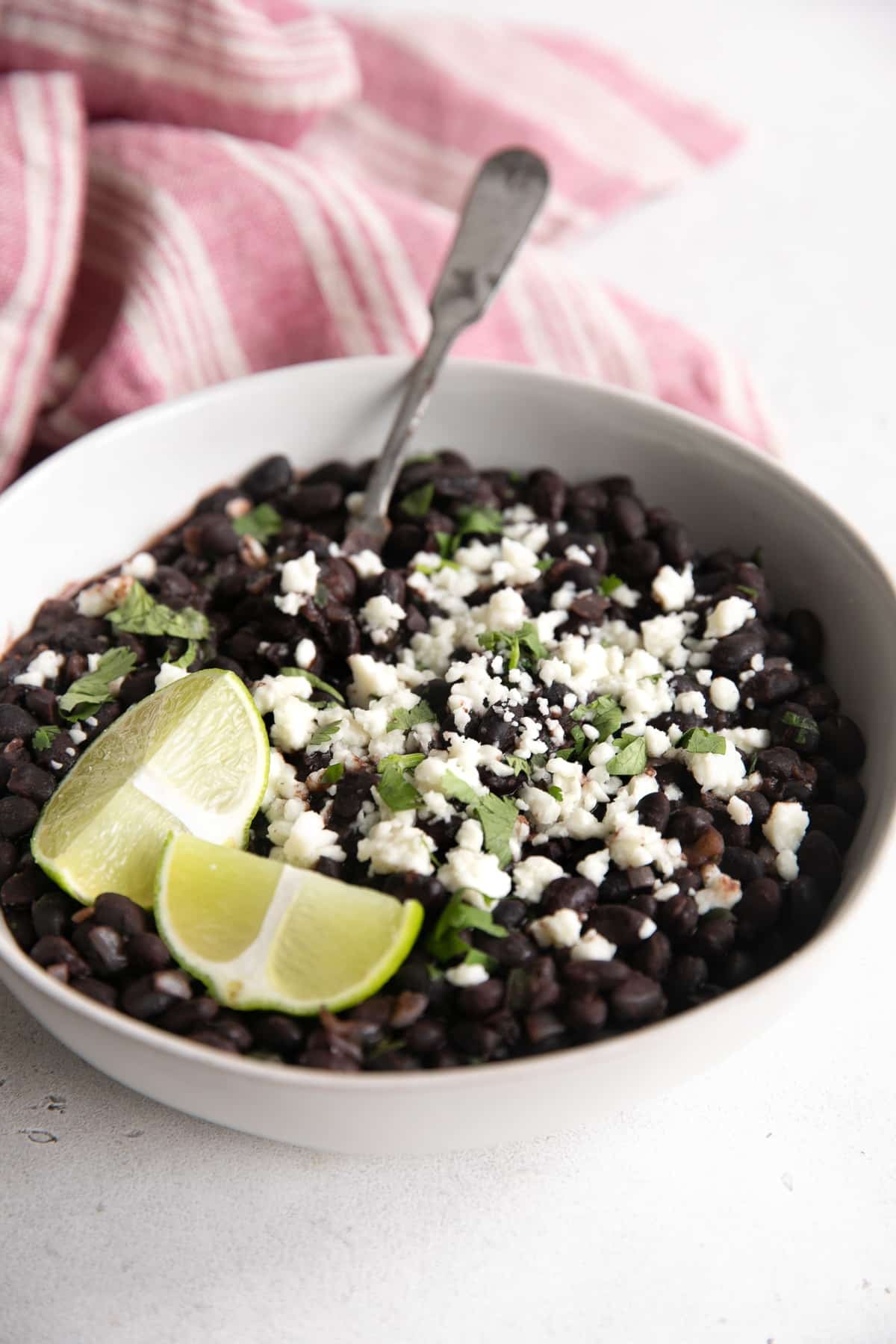 White bowl filled with Mexican-style black beans garnished with cotija cheese and fresh cilantro.