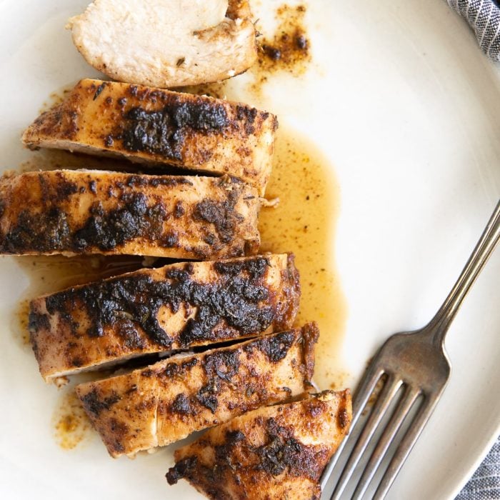 One blackened chicken breast on a white plate sliced into strips.