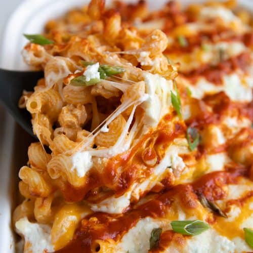 Scooping warm and gooey buffalo chicken pasta from a large baking dish.