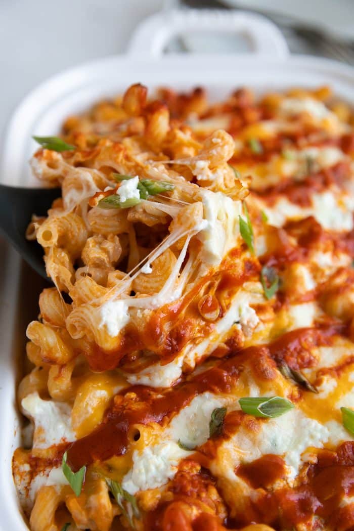 Scooping warm and gooey buffalo chicken pasta from a large baking dish.