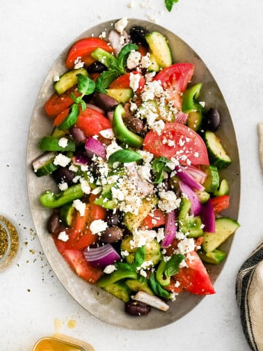 Traditional Greek salad served on a large white platter with crumbled feta on top.
