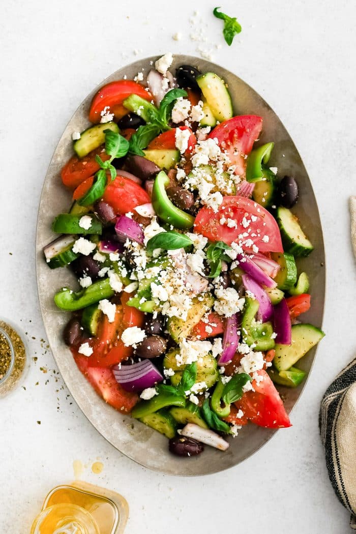 Traditional Greek salad served on a large white platter with crumbled feta on top.
