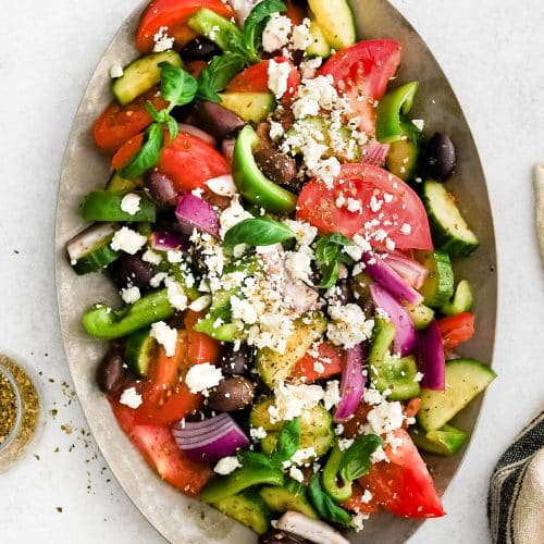 Traditional Greek salad served on a large white platter with crumbled feta on top.