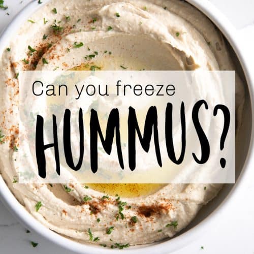 Image of a large white bowl filled with hummus with simple text overly with the question: can you freeze hummus?