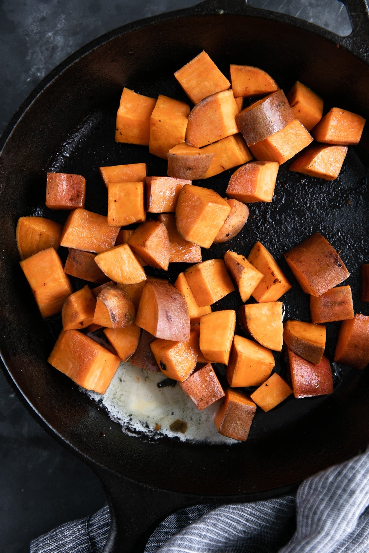 Cubes of sweet potato cooking in a large cast iron skillet.