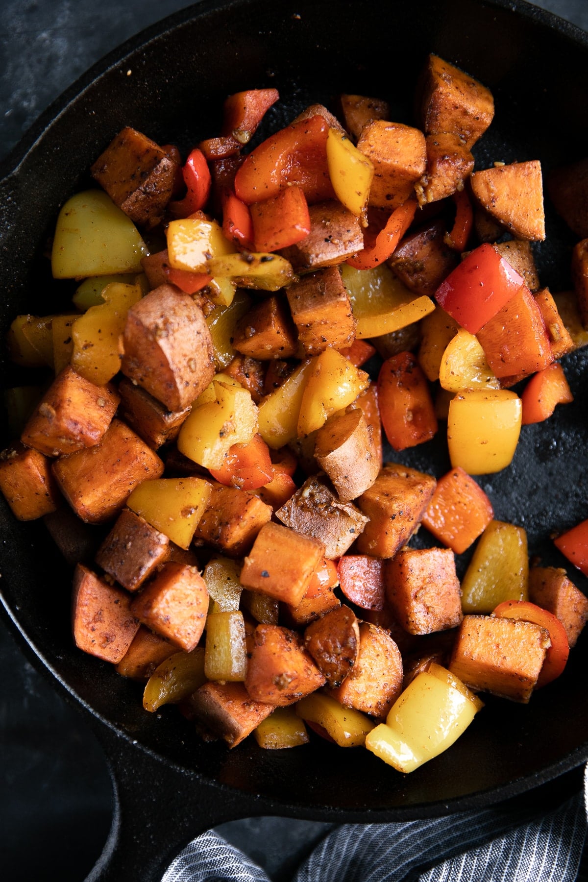 Sweet potatoes and bell peppers covered in cajun spices cooking in a cast iron skillet.