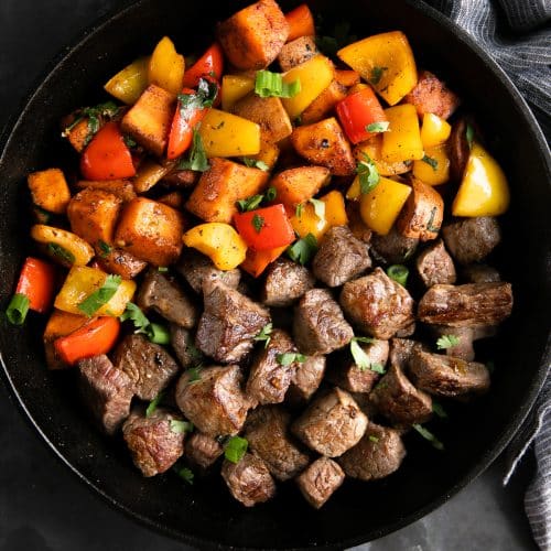 Large cast iron skillet filled with cooked steak bites and cajun spiced sweet potatoes and peppers.
