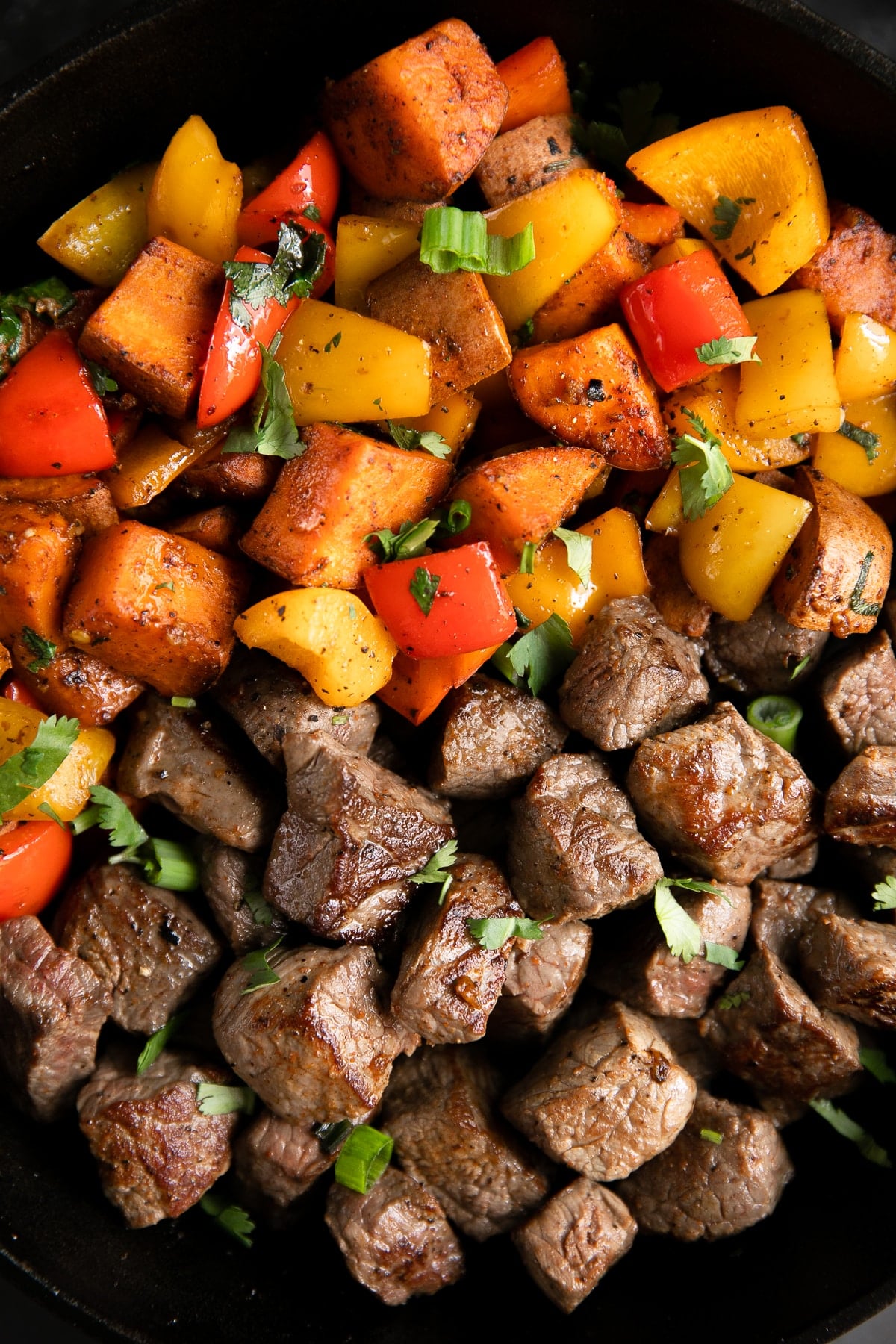 Large cast iron skillet filled with cooked steak bites and cajun spiced sweet potatoes and peppers.