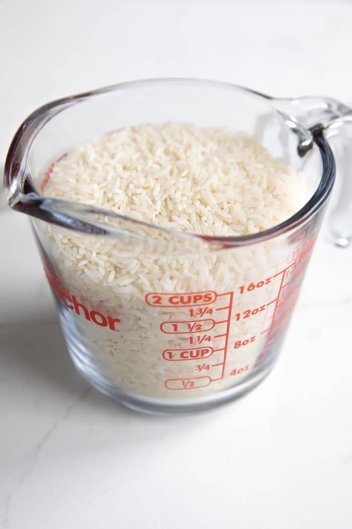 Glass measuring cup filled with uncooked white rice.