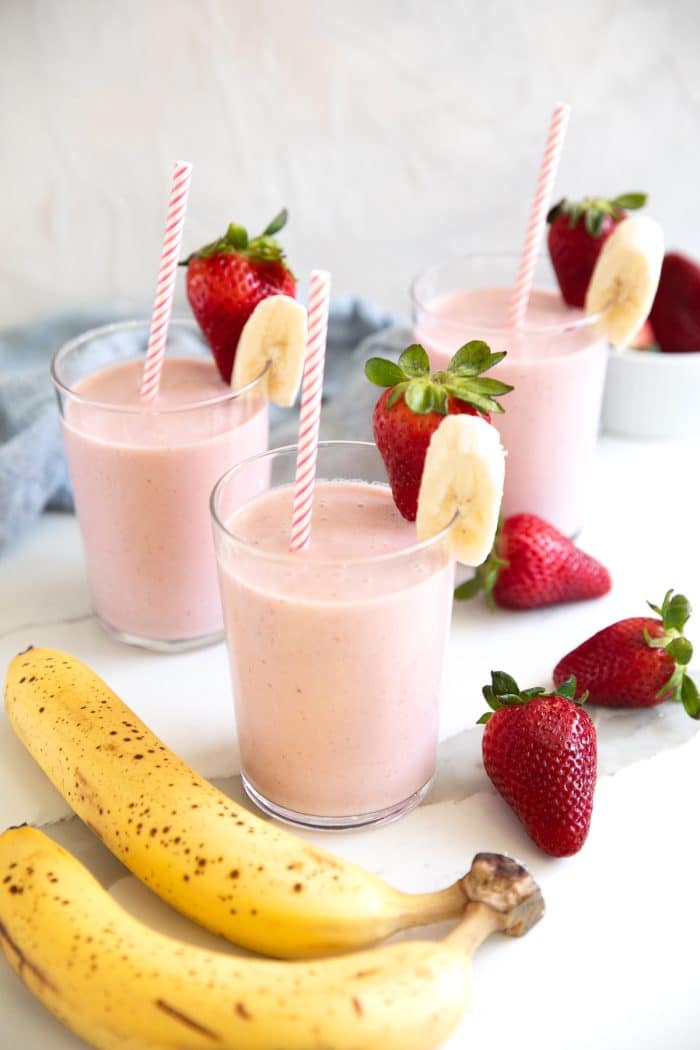 Three glasses with strawberry banana smoothie garnished with one strawberry and one banana slice.