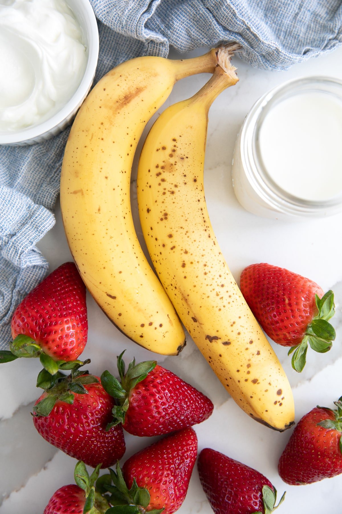 Ingredients for banana strawberry smoothie including bananas, strawberries, milk, and yogurt.