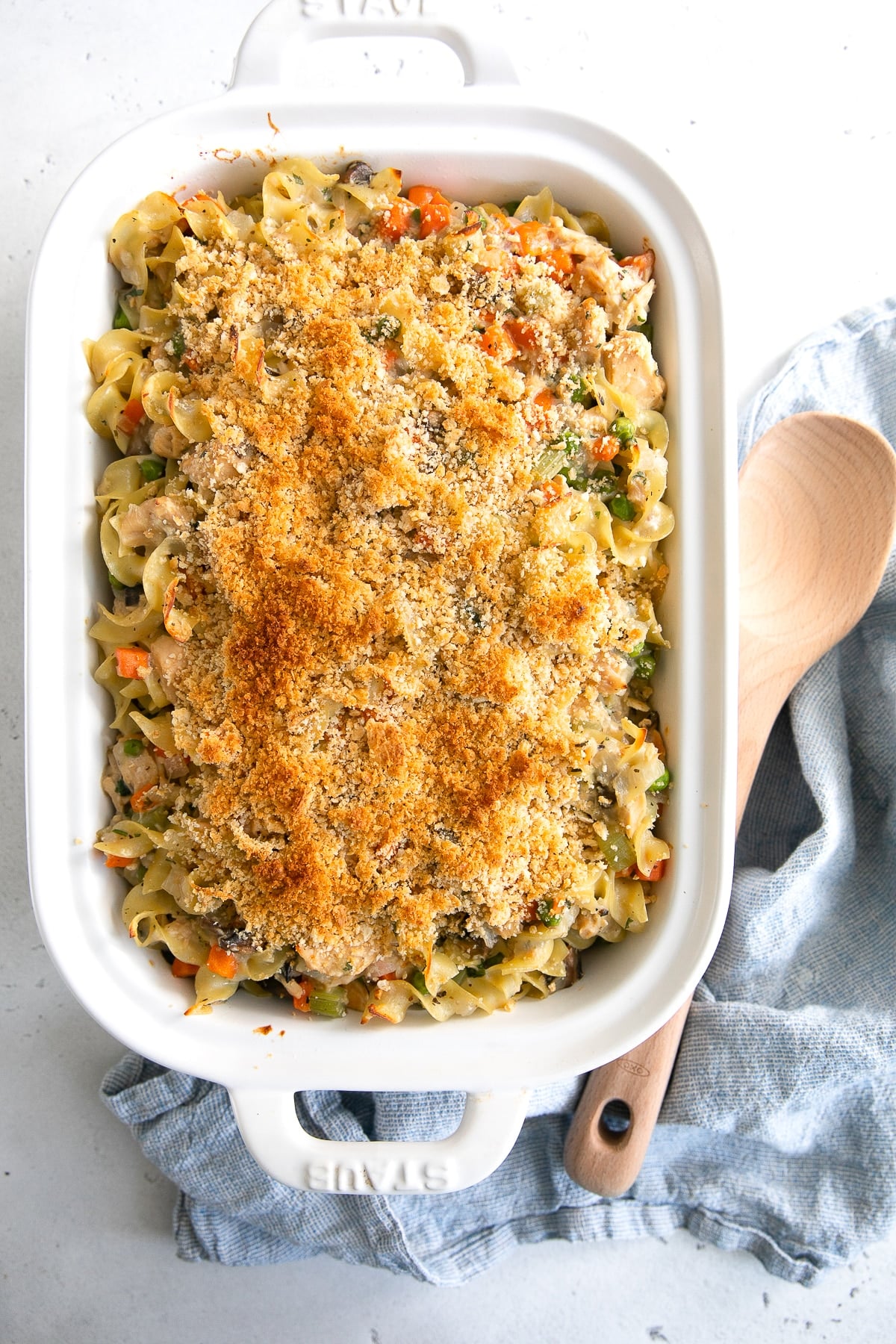 White baking dish filled with tuna noodle casserole and topped with crushed whole wheat Ritz crackers and butter.