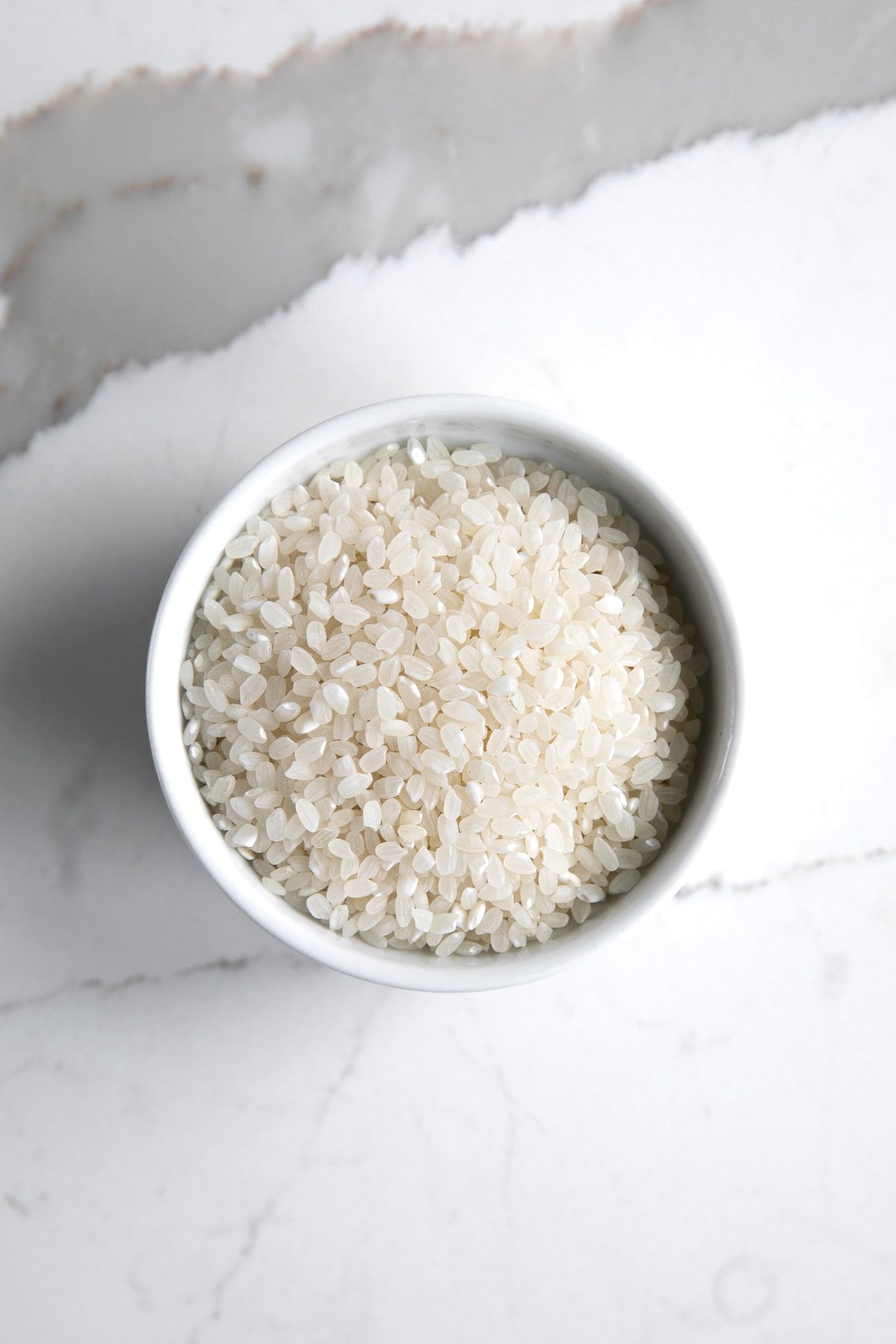 Small white bowl filled with uncooked sushi rice