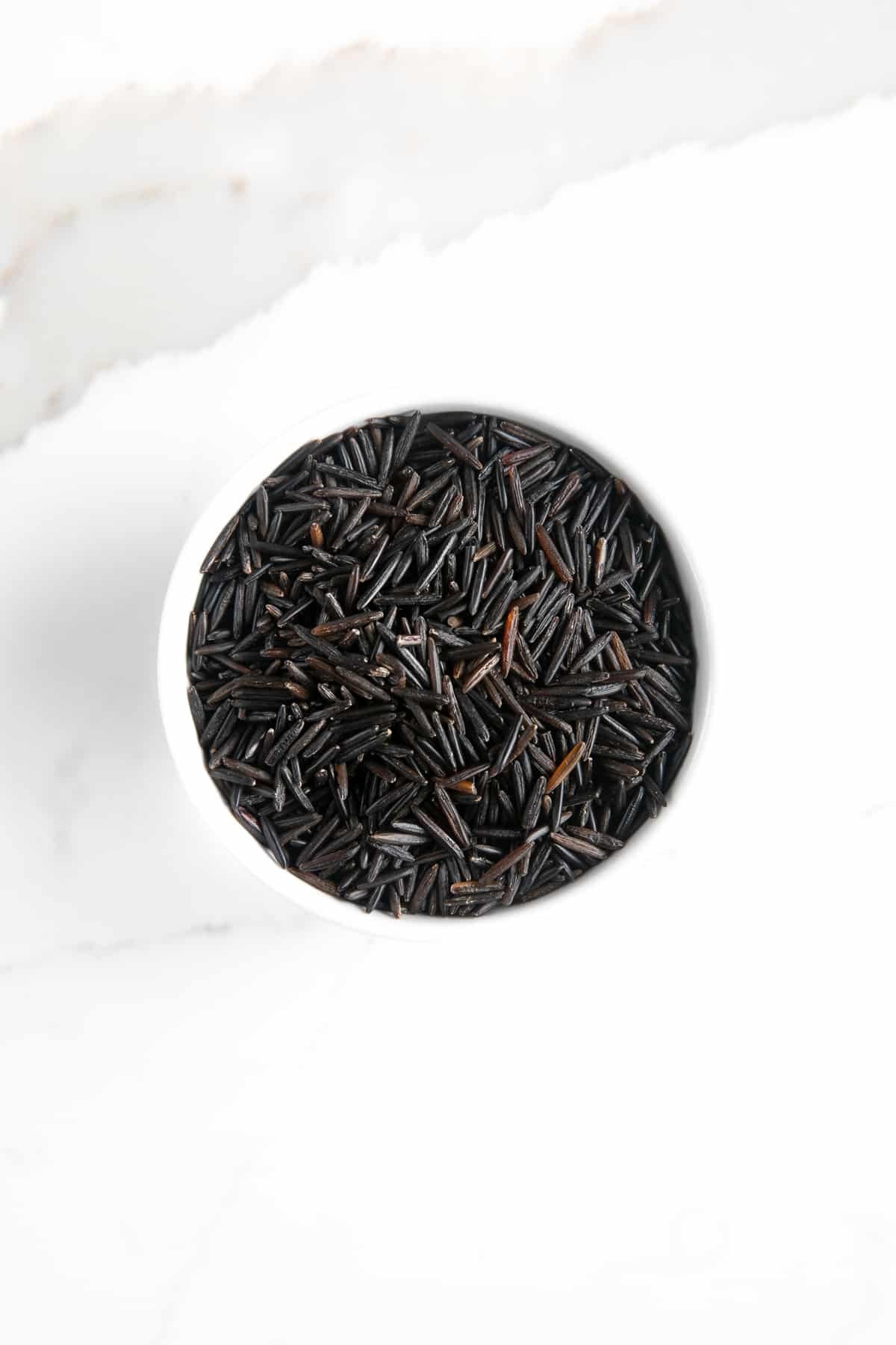 Uncooked wild rice in a white bowl.