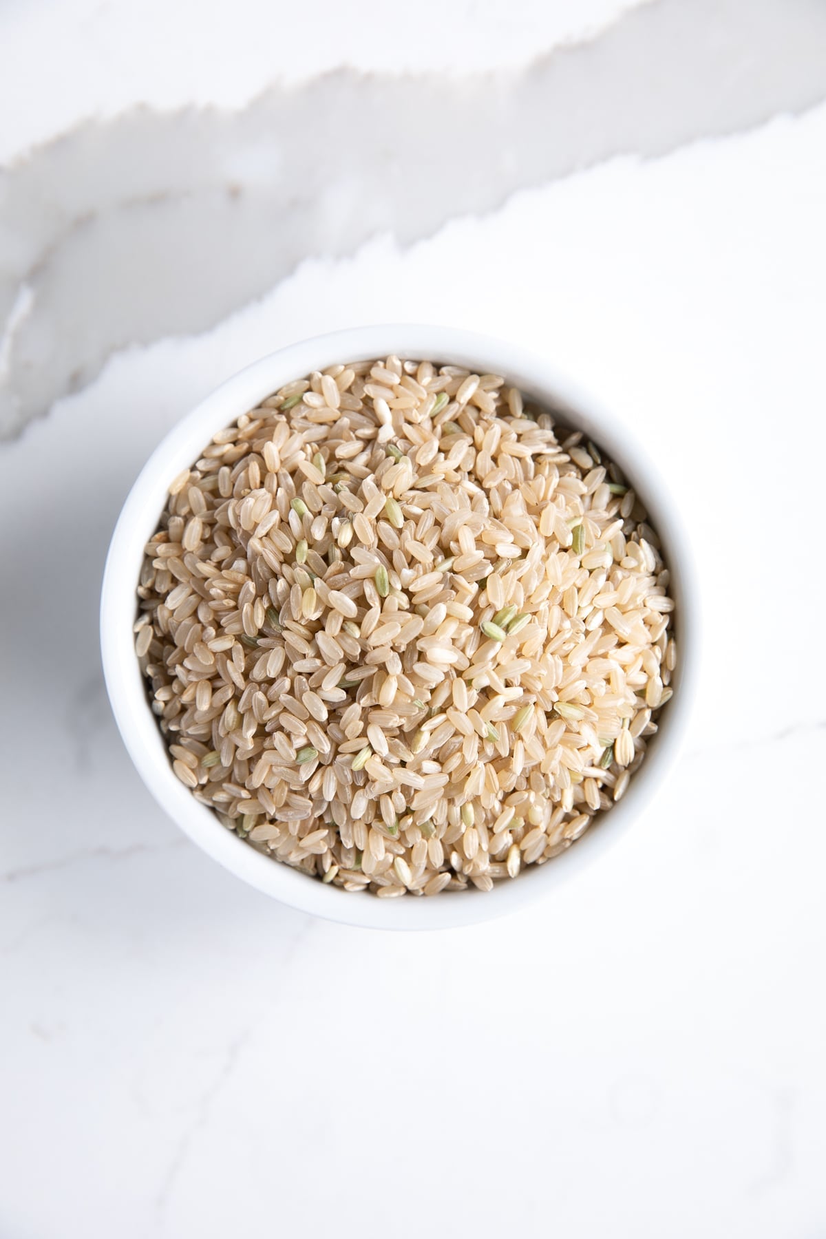 Uncooked short-grain brown rice in a small white bowl.