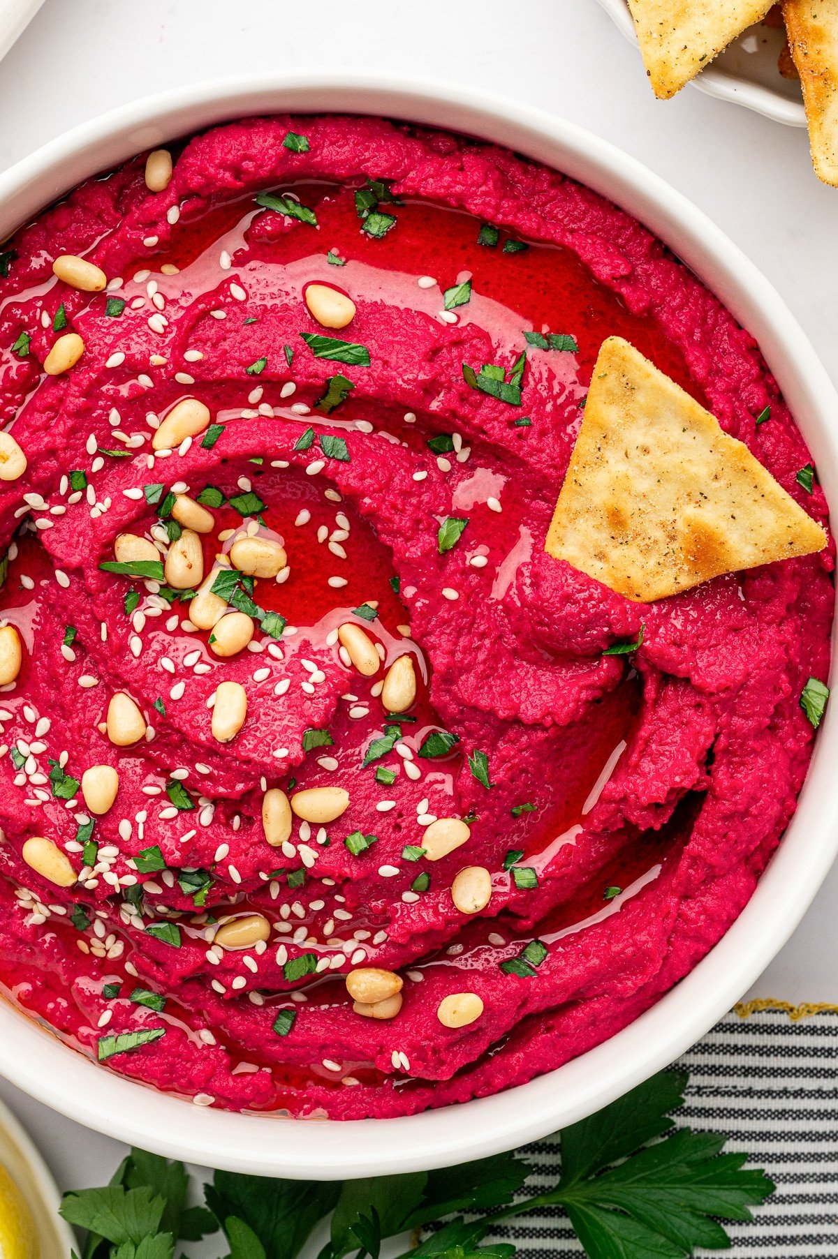 Vibrant pink beet hummus garnished with olive oil, sesame seeds, and pine nuts