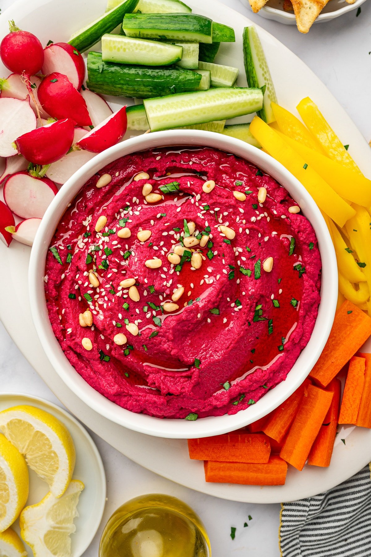 Creamy beet hummus served in a bowl with sliced cucumbers, radishes, bell peppers, and carrots.
