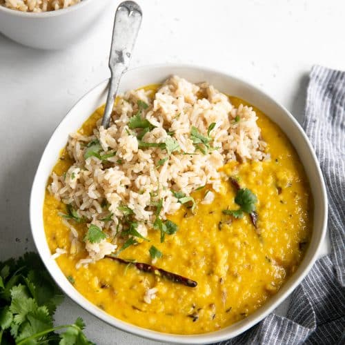 Large shallow bowl filled with Indian red dal served with brown rice and cilantro.