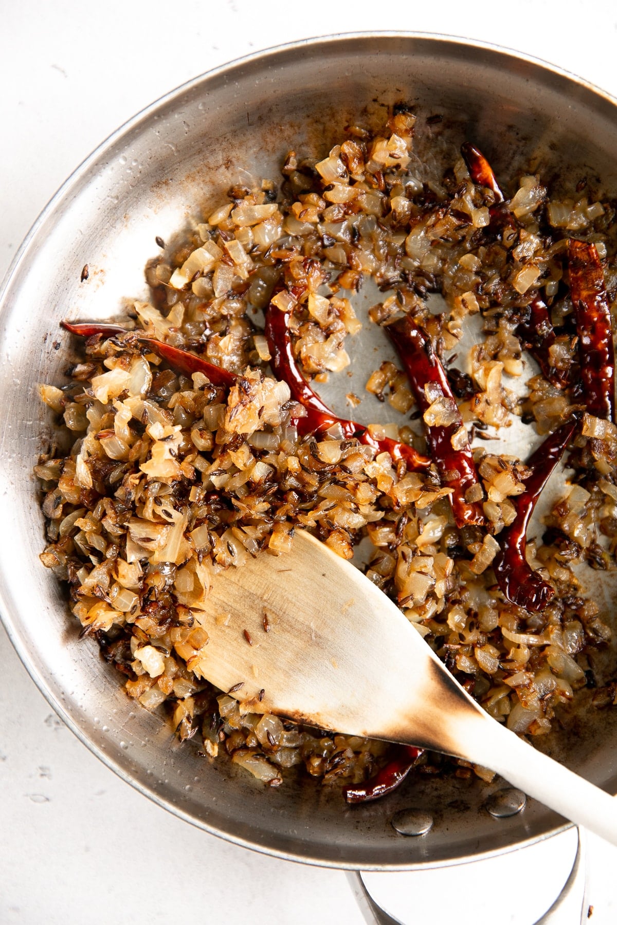 Frying chopped onion, cumin seeds, and dried red chilis in oil.