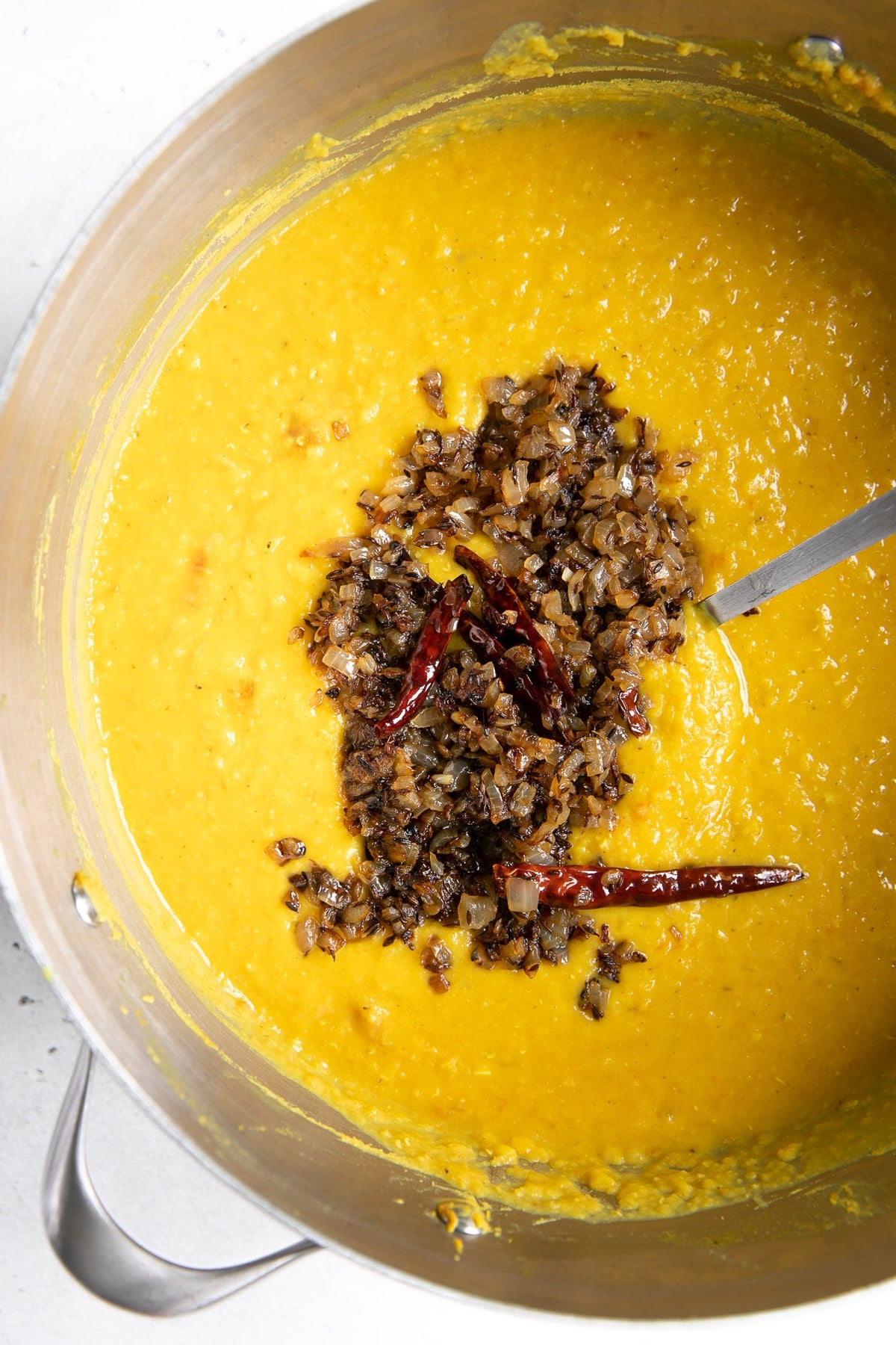 Large pot filled with cooked Indian Masoor Dal and topped with browned onions, cumin seeds, and dried red chilis.