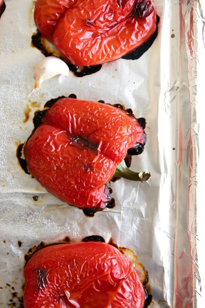 Charred roasted red bell peppers and garlic on a baking sheet after broiling