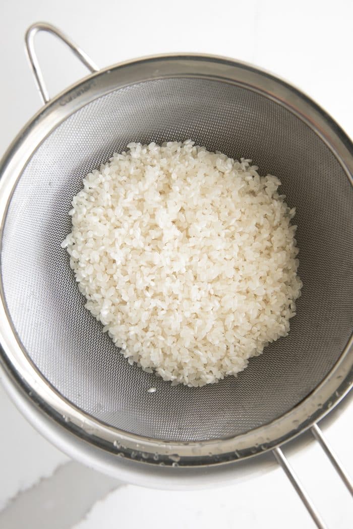 Washed glutinous rice straining in a fine-mesh strainer.