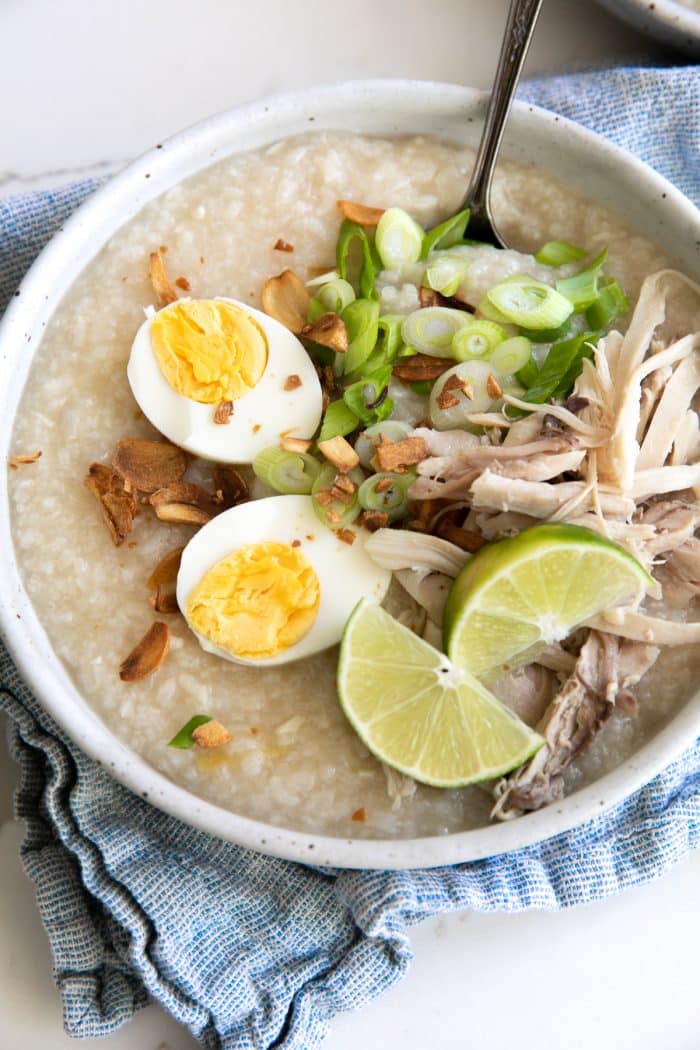 Bowls filled with cooked arroz caldo and garnished with fried garlic, scallions, hard-boiled egg, and shredded chicken.