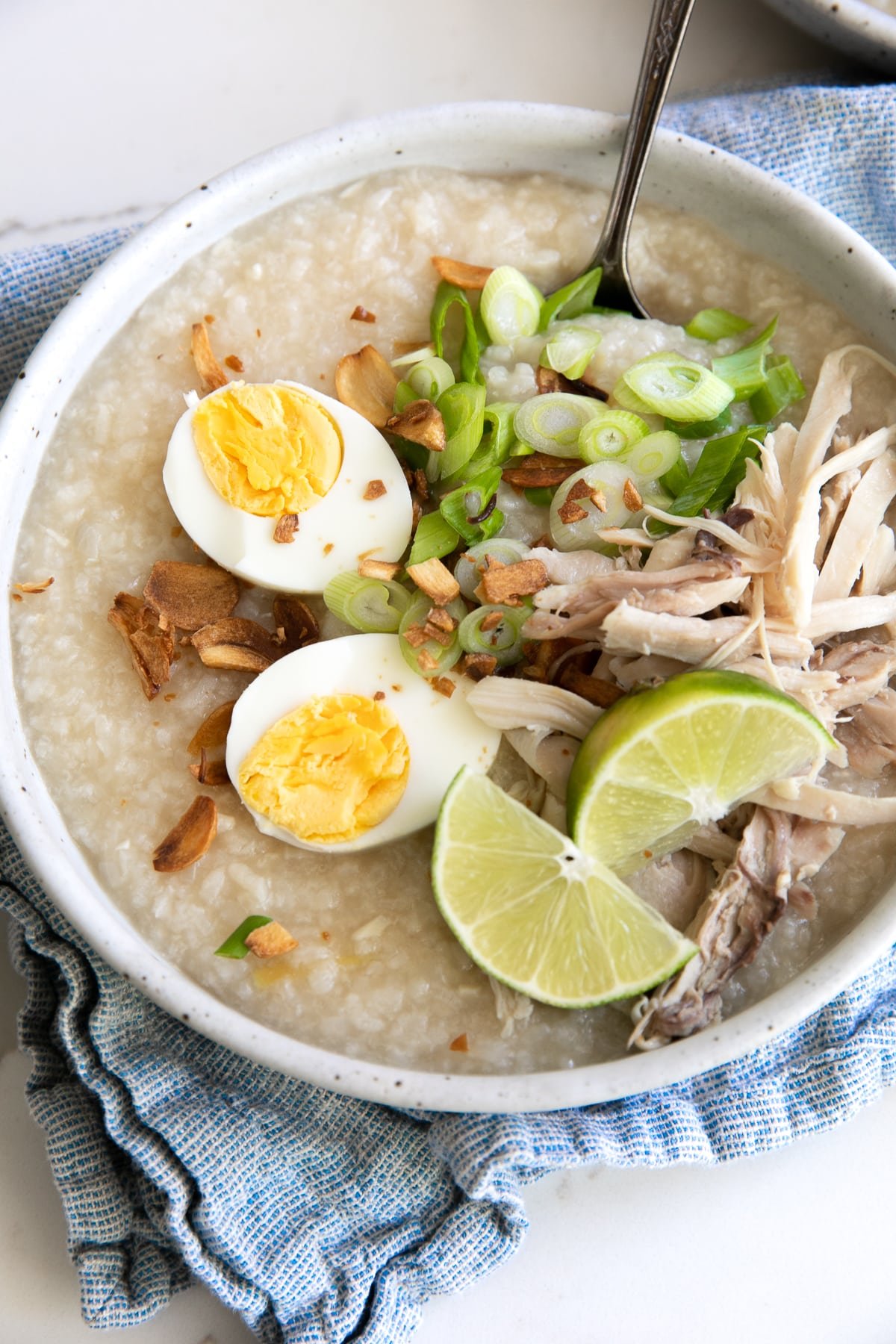 Bowls filled with cooked arroz caldo and garnished with fried garlic, scallions, hard-boiled egg, and shredded chicken.