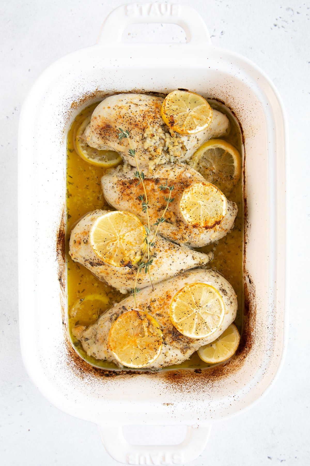 Four large chicken breasts in a white baking dish cooked in a buttery lemon, garlic, and herb sauce.
