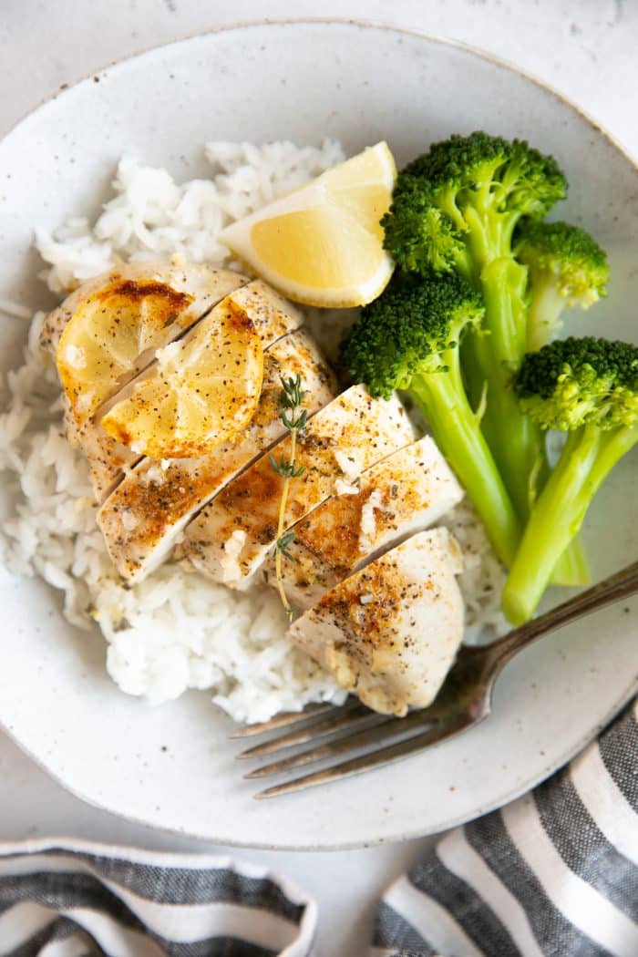 Juicy baked lemon chicken breast served on top of white rice with a side of cooked broccoli.