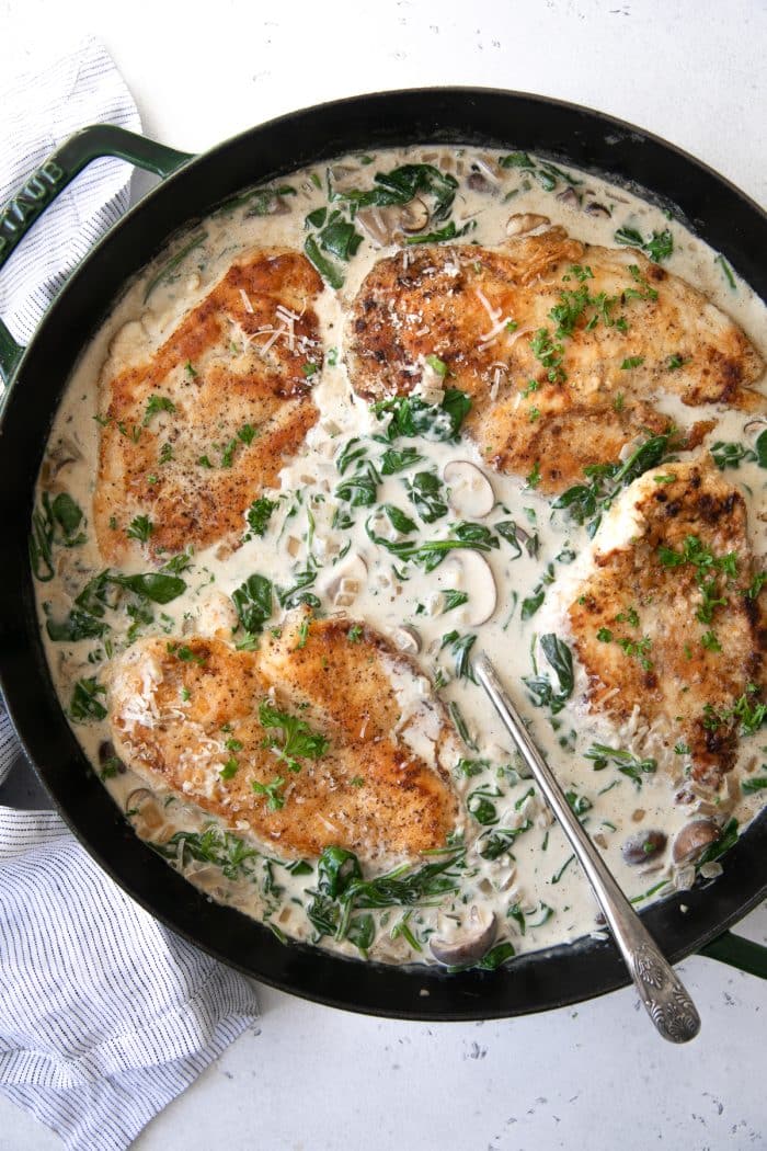 Large skillet filled with cooked chicken breasts in a creamy mushroom and spinach florentine sauce.