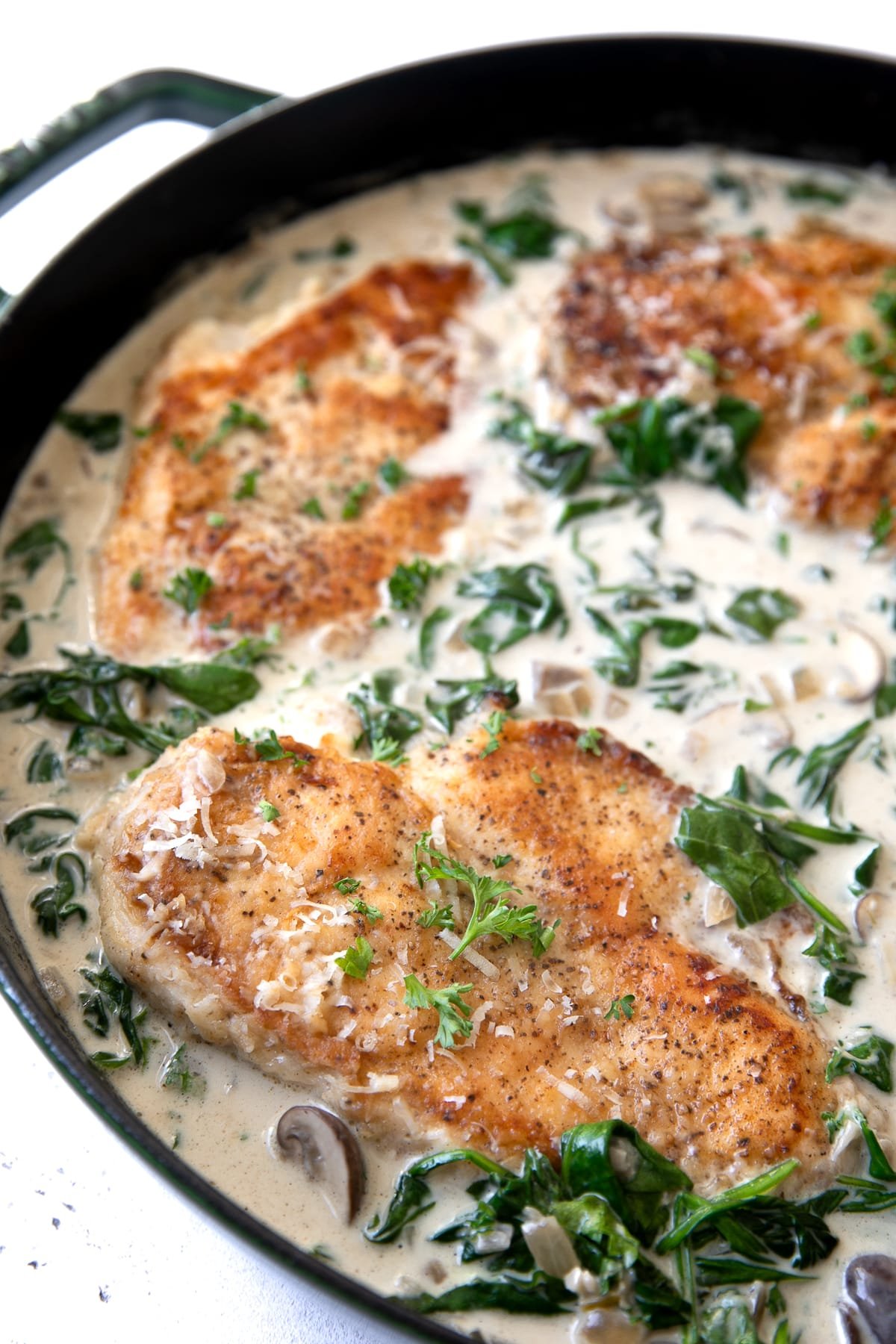 Lightly floured and fried chicken breast in a large skillet filled with a homemade spinach, mushroom, and cream sauce.
